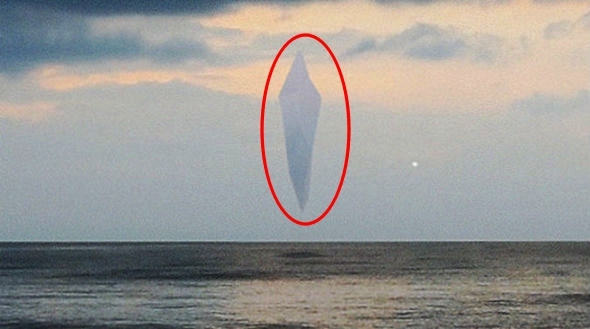 Hình ảnh cắt từ đoạn clip cho thấy vật thể bay có hình dạng thon dài thẳng đứng và bao quanh bởi đám mây xanh.