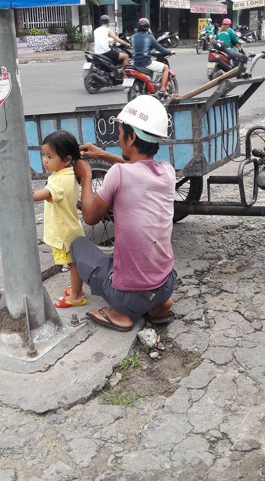 
Người bố công nhân cẩn thận thắt bím tóc cho cô con gái - Ảnh: Huỳnh KoKo