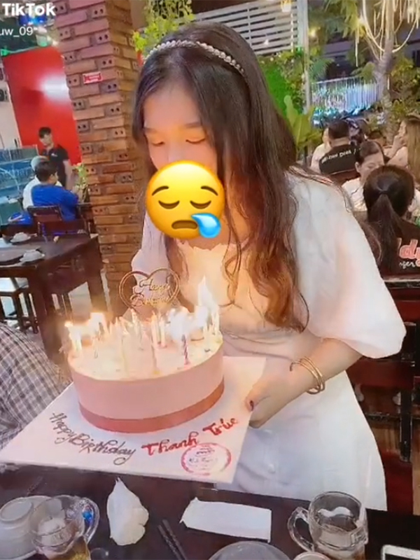 Cô gái đang thổi nến trên chiếc bánh sinh nhật thật đẹp, và mọi người xung quanh đang chúc mừng cô ấy bằng cách hát \
