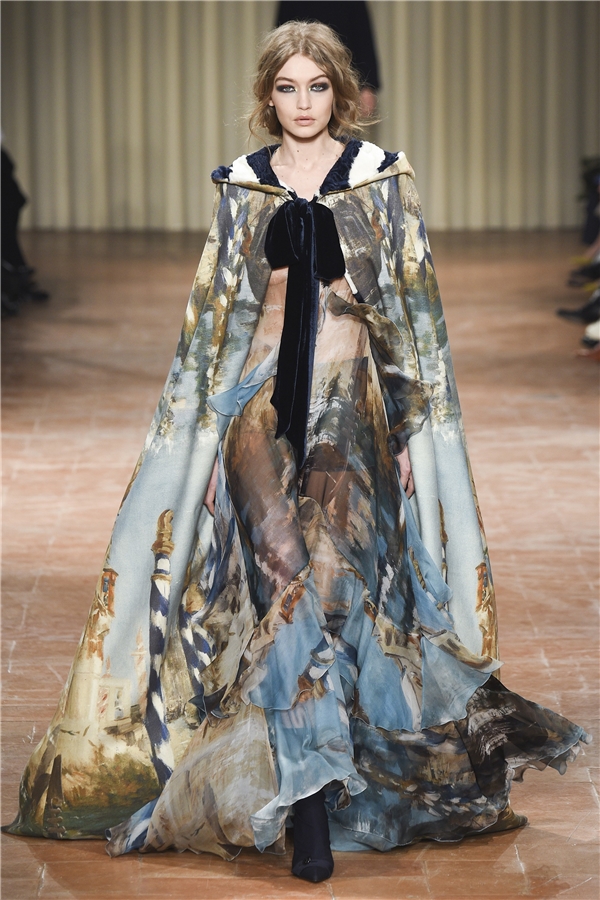
Gigi Hadid nhận vai trò mở màn cho bộ sưu tập này. Phô diện bộ váy trên nền voan lụa mỏng manh, gây ấn tượng bởi họa tiết in tái hiện những công trình kiến trúc cổ điển của châu Âu. Vòng một của chân dài gần như phô diễn trọn vẹn.
