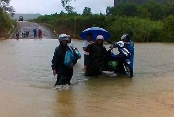 Người dân phải khiêng xe máy qua đoạn đường ngập. Ảnh: Báo Quảng Bình.