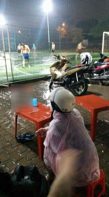 
Mặc trời mưa to, cô vợ mặc áo mưa đợi chồng đá bóng.
