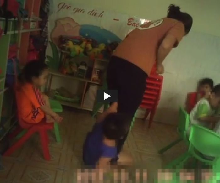 
Một cô giáo đang kéo chân của cháu bé để đánh vào bàn chân (ảnh: cắt từ clip)