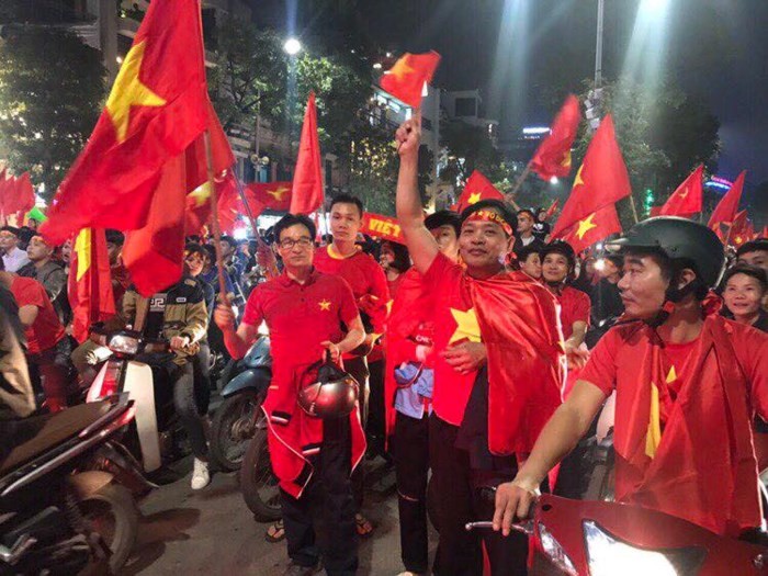 
Phó Thủ tướng giản dị với chiếc áo thun có ngôi sao vàng bên ngực trái, tay cầm lá cờ Tổ quốc hòa chung không khí ăn mừng với người hâm mộ.