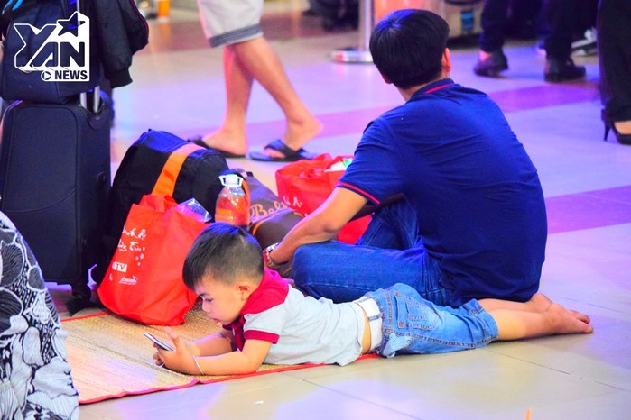 
Một em nhỏ nằm dài trên chiếc chiếu trải trên sàn nhà để chơi smartphone trong khi cùng gia đình chờ tàu đến.