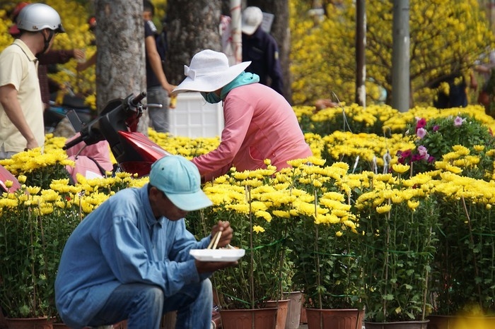 Người nông dân ăn vội hộp cơm  dưới cái nắng gắt trước khi chia tay Sài Gòn hoa lệ, kết thúc những ngày ăn ngủ cùng hoa Tết để trở về nhà chuẩn bị đón giao thừa