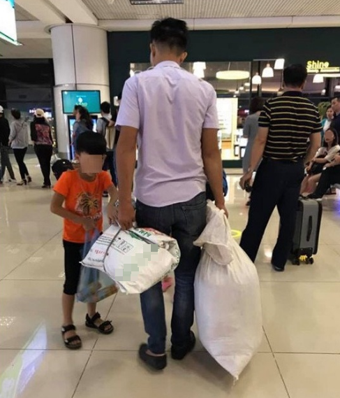  
Hình ảnh hai bố con dùng bao tải đựng hành lý ở sân bay. 
