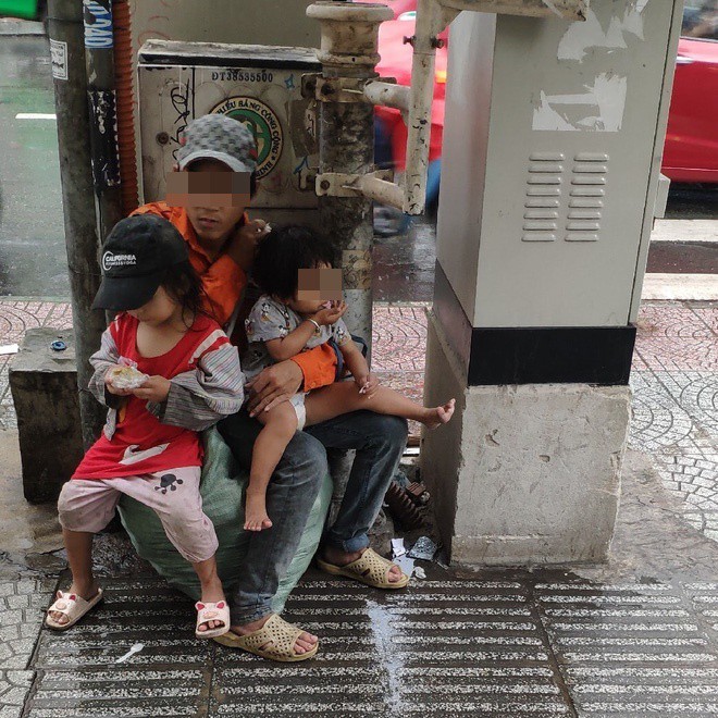  
Hình ảnh người cha lam lũ đang bế hai cô con gái nhỏ của mình núp mưa