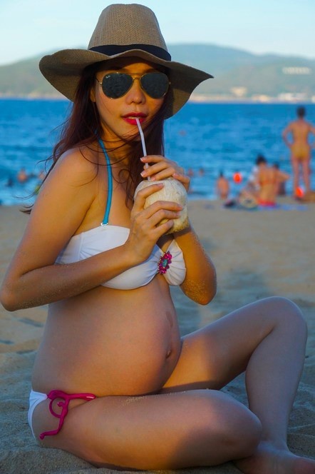  
Kiwi Ngô Mai Trang tự nhiên uống dừa, ngồi tận hưởng không khí biển với "bụng bầu vượt mặt". (Ảnh: FBNV)