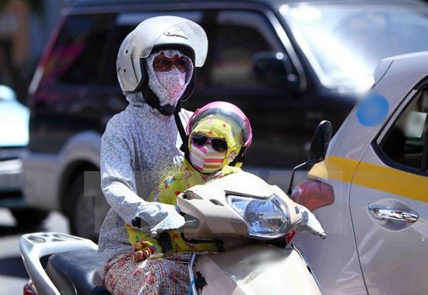  
Hình ảnh một em bé được mẹ mặc áo chống nắng chở trên xe máy. (Ảnh: TTXVN)