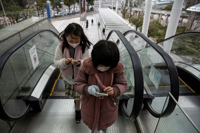  
2 cô gái trẻ dán mắt vào điện thoại khi đi thang cuốn ở Nhật (Ảnh: Reuters)