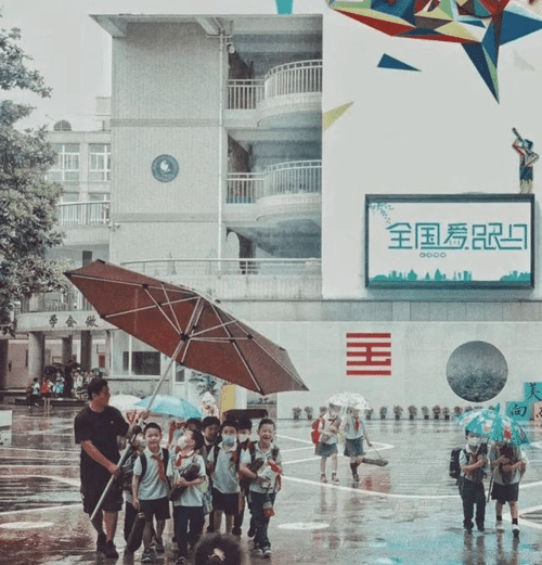  
Thầy giáo dùng ô để che cho học sinh. (Ảnh: China Daily)