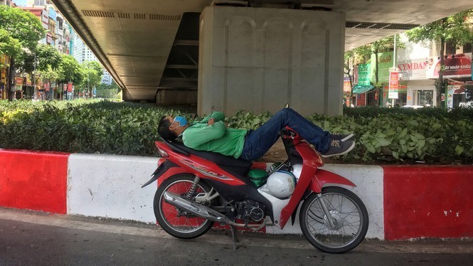  
Một tài xế công nghệ nghỉ chân dưới gầm cầu để tránh nắng (Ảnh: Tiền Phong)