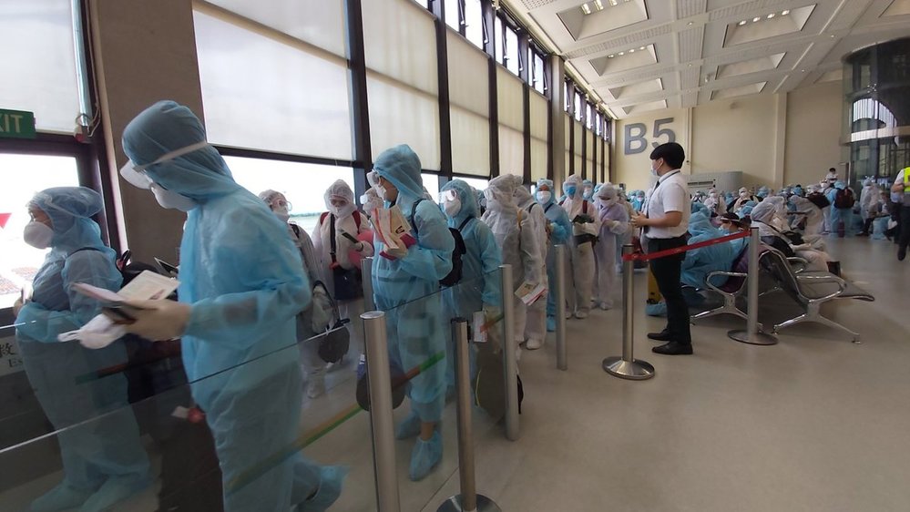  
Các công dân Việt Nam ở nước ngoài mặc đồ bảo hộ và xếp hàng làm thủ tục (Ảnh: VNExpress)