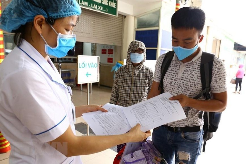 
Nhân viên y tế hướng dẫn mọi người điền tờ khai y tế (Ảnh: TTXVN)