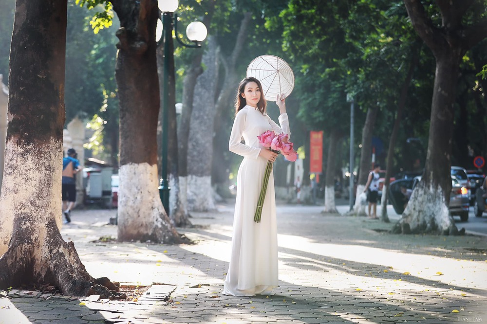  
Tà áo dài cùng nón lá, sen hồng khiến cho khung cảnh trên con phố Phan Đình Phùng trở nên lãng mạn hơn. (Ảnh: Nguyễn Ngọc Kiều)