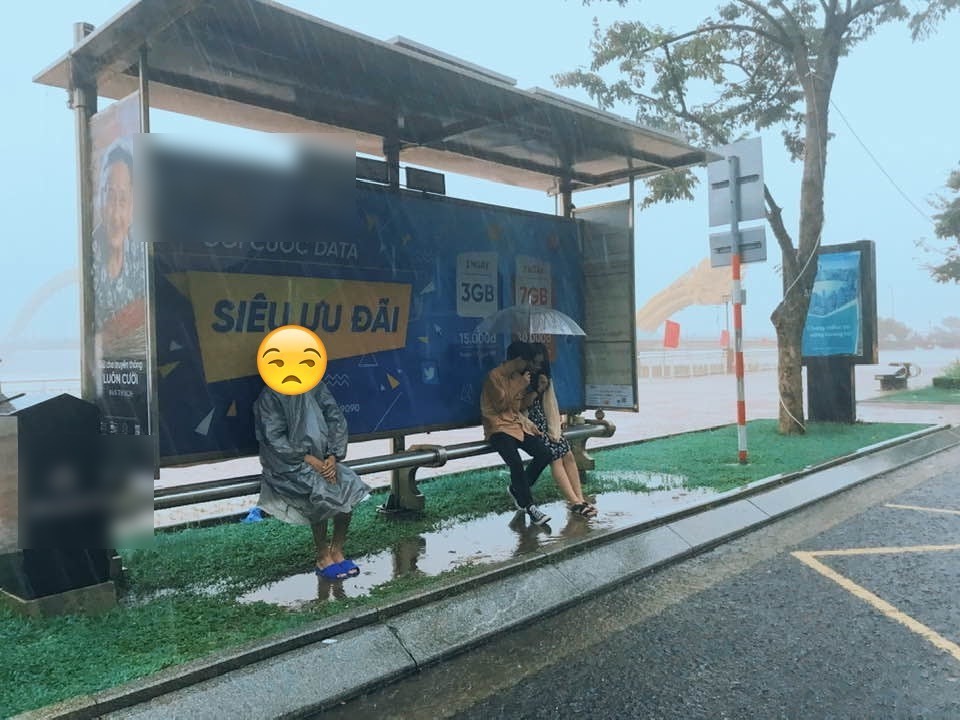 
Thanh niên áo mưa xám trú cùng với cặp đôi che ô trong trạm chờ xe buýt ngày mưa lớn. (Ảnh: S.V.Đ.N CFS/ P.A 73)