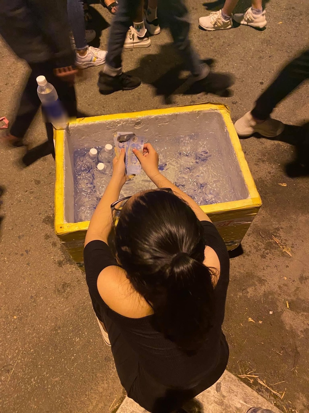  
Cô gái ngồi xổm bên thùng nước suối giúp đỡ chú bán hàng rong. (Ảnh: FB H.Y)