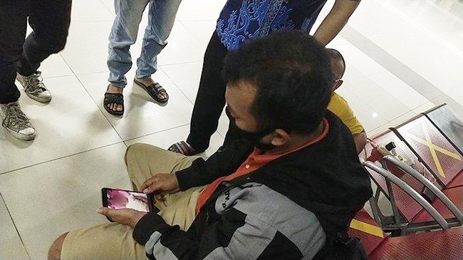  
Người đàn ông thất thần nhìn ảnh đứa con mới sinh trong điện thoại (Ảnh: Tribunnews)