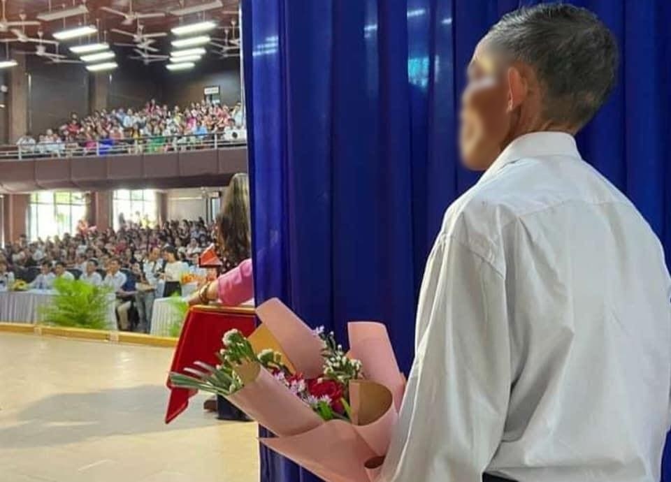  
Ông bố đứng nép mình trong cánh gà, ôm bó hoa đợi con gái tại buổi lễ tốt nghiệp. (Ảnh: FB N.T.C.M)