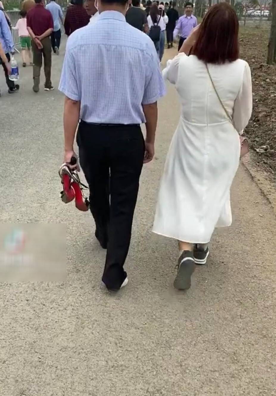  Người đàn ông đi chân không, đeo tất, tay thì xách giày cao gót và để cho vợ đi giày của mình. (Ảnh cắt từ clip)