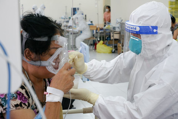  
Một tình nguyện viên từng là F0 đang giúp bệnh nhân sử dụng mặt nạ oxy. (Ảnh: Tuổi Trẻ)