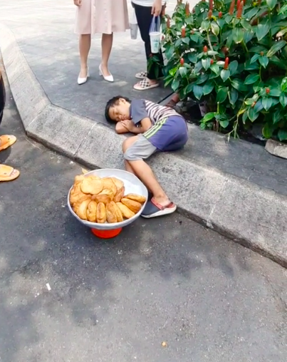  
Cậu bé bán bánh mì ngủ quên trên vỉa hè Sài Gòn. (Ảnh: Trần Quang Hùng)