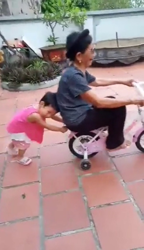  
Cụ bà hào hứng ngồi trên chiếc xe đạp để cháu đẩy quanh sân. (Ảnh: Cắt từ clip L.A.T)