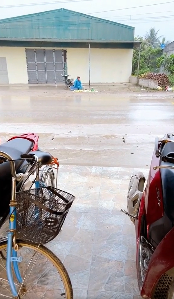  
Người nông dân ngồi bán hàng giữa mưa. (Ảnh: A.T)